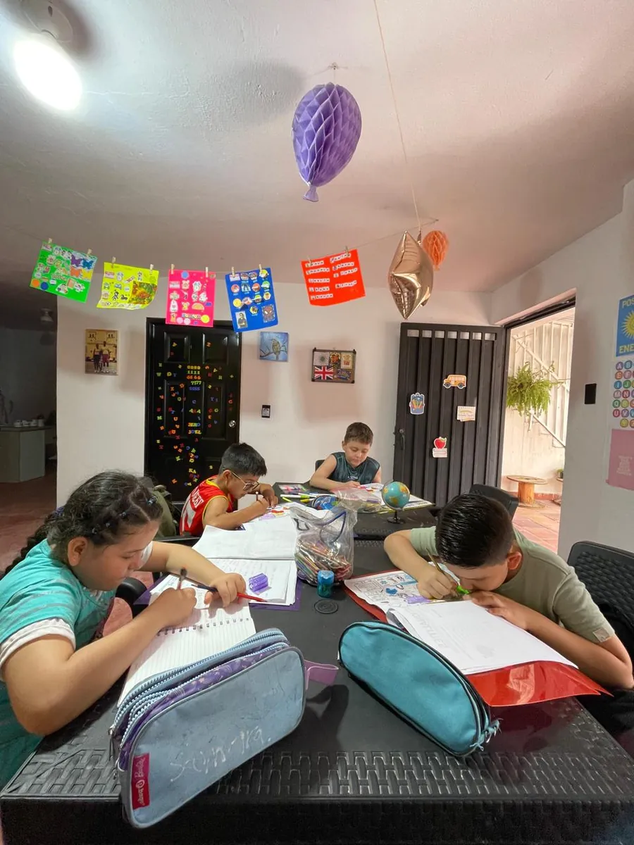 Aula decorada con banderines donde niñas y niños trabajan en sus cuadernos